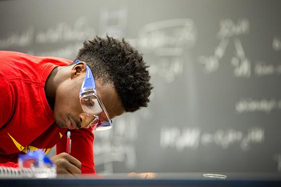 照片中的学生戴着护目镜，在实验室工作