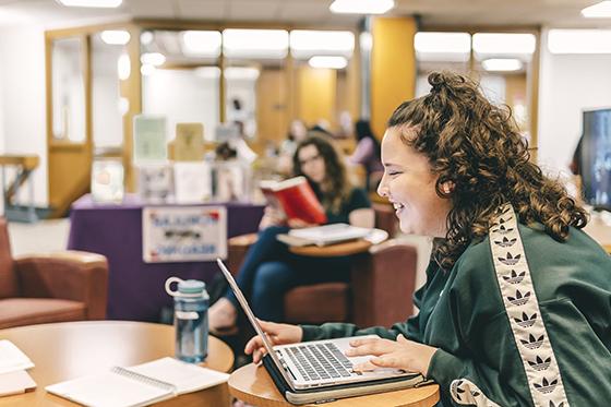 图为一名波胆网站的女学生在珍妮·梅隆·金图书馆的桌子旁工作时微笑的照片.