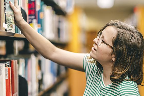Photo of a female Chatham University student taking a book off of a library shelf
